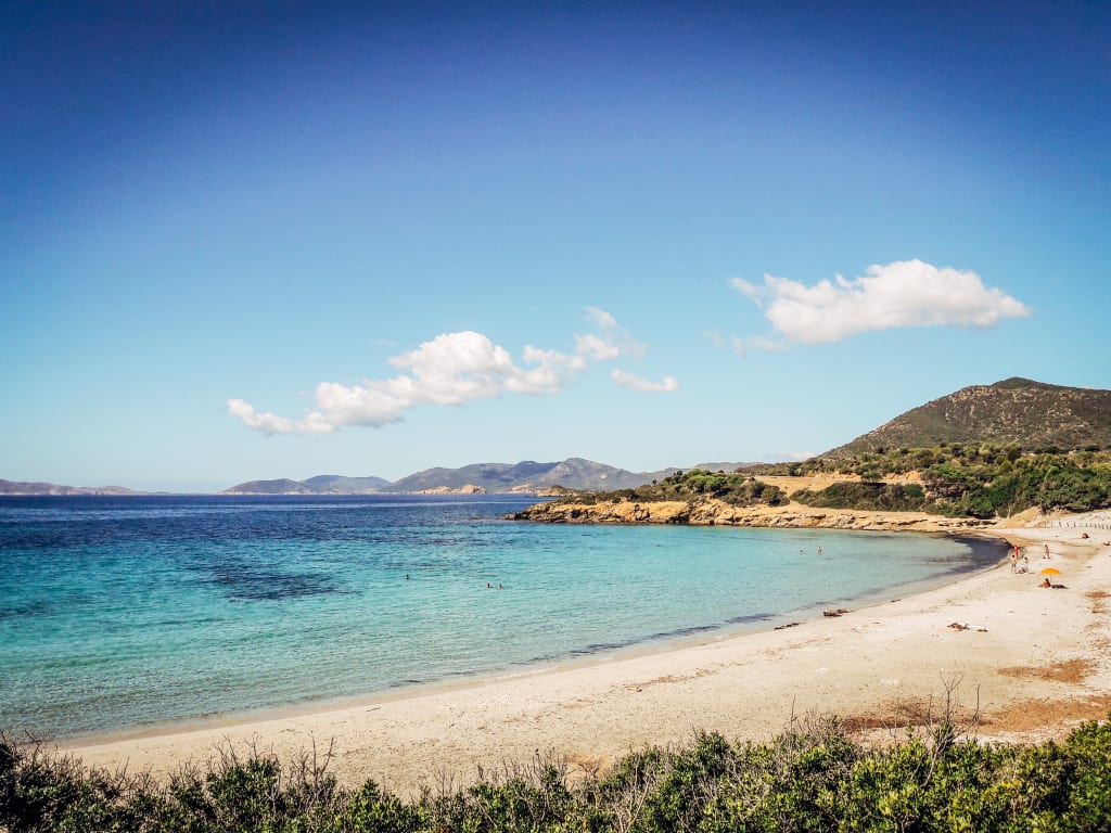 Spiaggia sabbiosa con acqua cristallina e colline sullo sfondo, Sardegna, il Sud-Ovest selvaggio