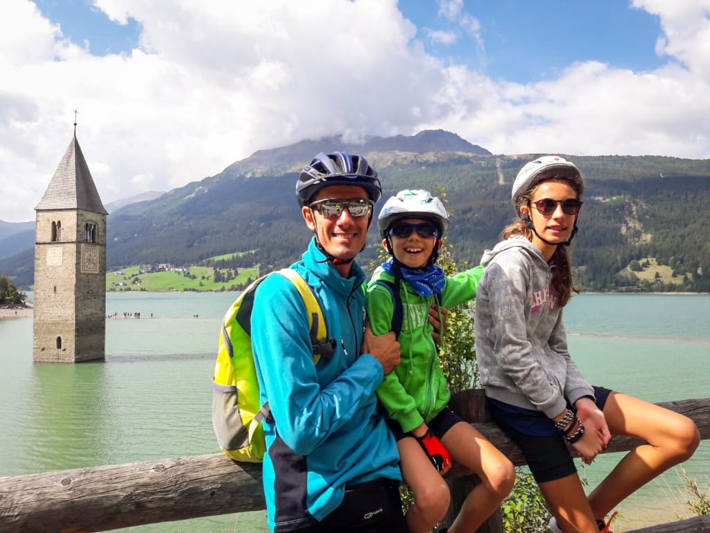 Family cycling near Lake Resia and the submerged bell tower, South Tyrol.