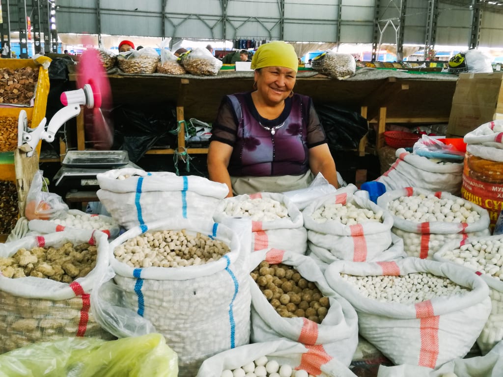 Mercato locale in Kirghizistan con venditrice che espone spezie e prodotti secchi in sacchi colorati.