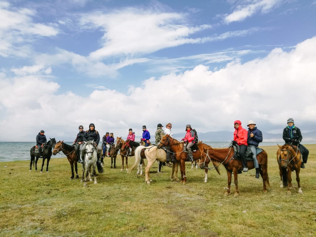 Gruppo di turisti a cavallo fermi in mezzo alla steppa con vasto paesaggio verde e cielo blu, Kirghizistan