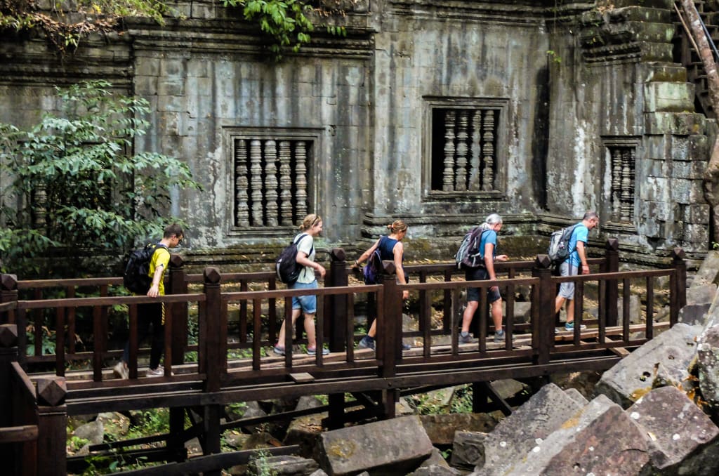 Escursionisti sul ponte di legno verso le rovine del tempio Ta Nei immerso nella foresta di Angkor