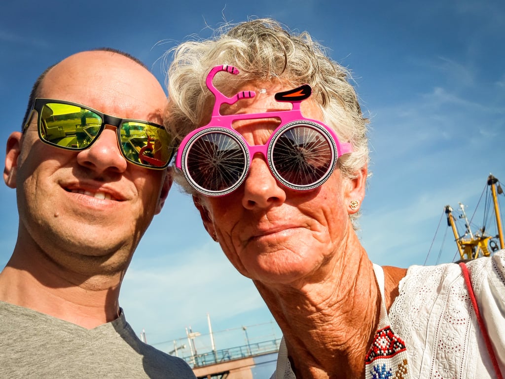 Coppia che si scatta un selfie con occhiali colorati e mulini a vento sullo sfondo a Zaanse Schans, Paesi Bassi.