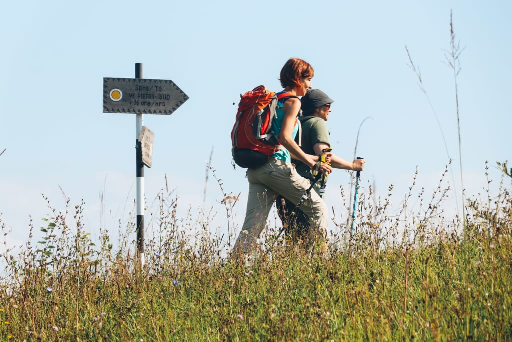 Due escursionisti passano vicino a un cartello con segnaletica lungo un percorso a piedi nelle montagne della Romania