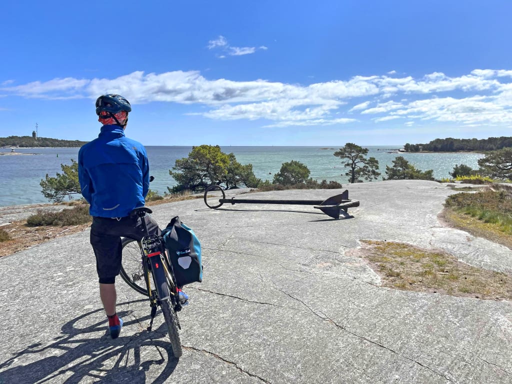 Ciclista con bici da viaggio lungo una strada costiera della Svezia, paesaggio nordico e mare.