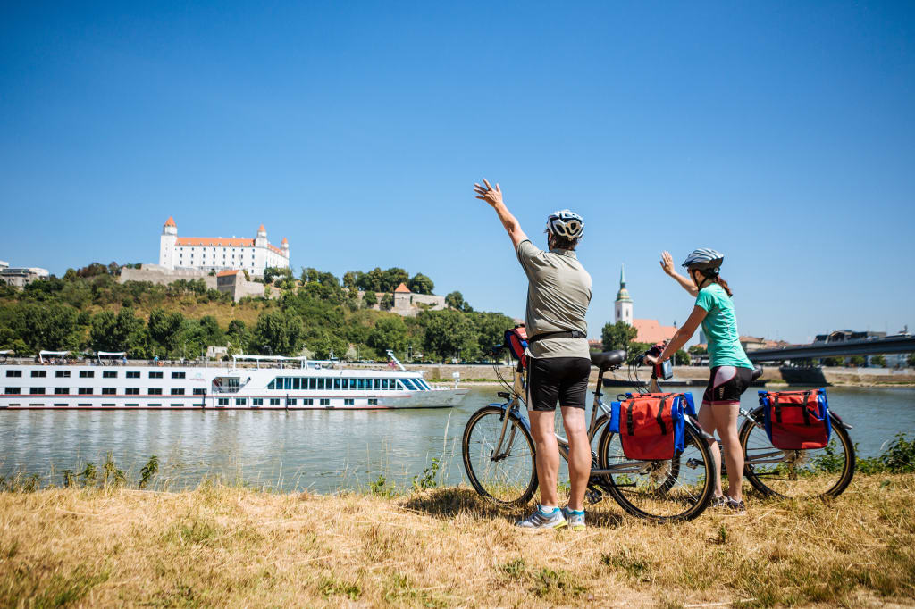 Due ciclisti salutano la barca passare in navigazione lungo il Danubio