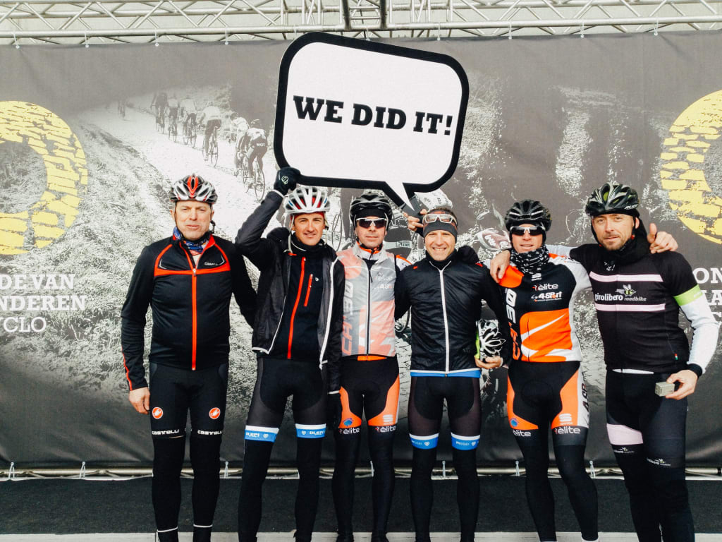 Gruppo di ciclisti che festeggiano con un cartello "We did it", evento ciclistico Fiandre