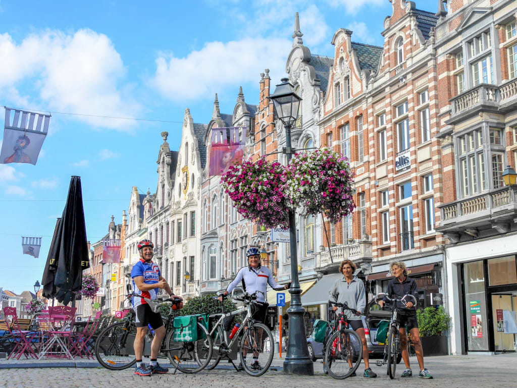 Strada pedonale con edifici storici e fiori appesi nelle Fiandre. viaggi in gruppo con Girolibero.