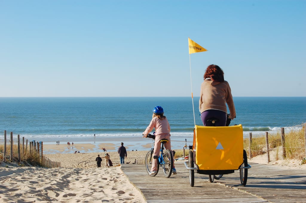 Famiglia in bici in un sentiero in legno sulla spiaggia tra le dune di sabbia ad Arcachon, Francia