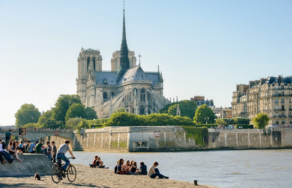 Vista della Cattedrale di Notre-Dame dalla sponda della Senna con persone sedute lungo la Senna, Parigi
