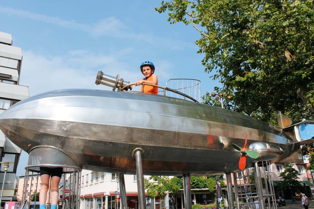 Bambino che gioca con una fontana moderna sul lungolago in Svizzera durante una vacanza attiva in famiglia