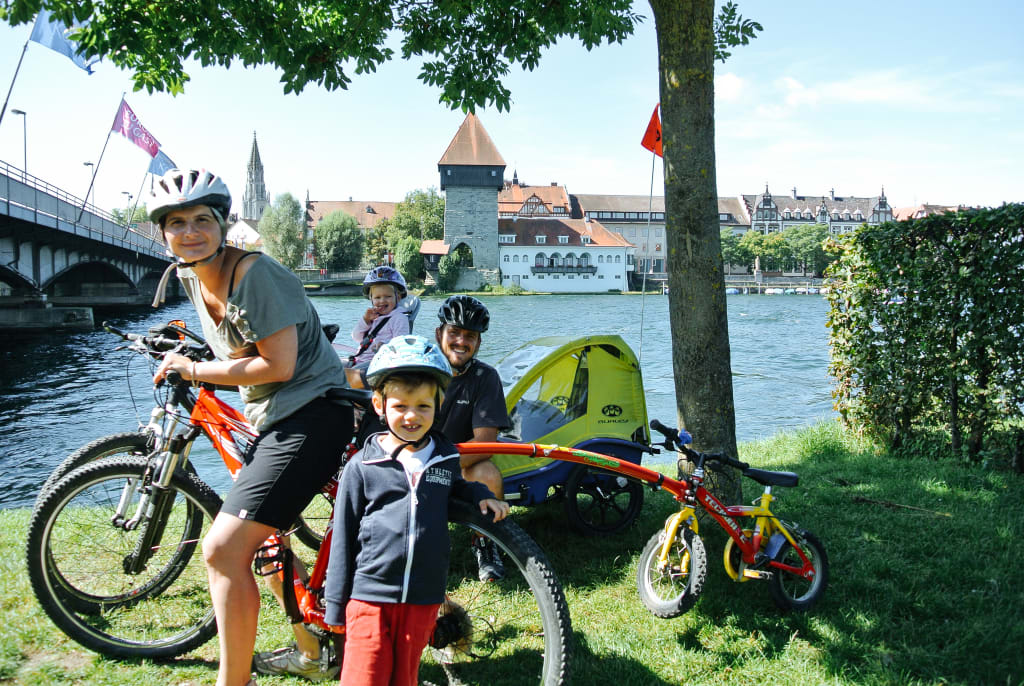 Famiglia di cicloturisti con caschetto, viaggiare in sicurezza, bici con carrellino, bici bimbo, cammellino, lago di Costanza