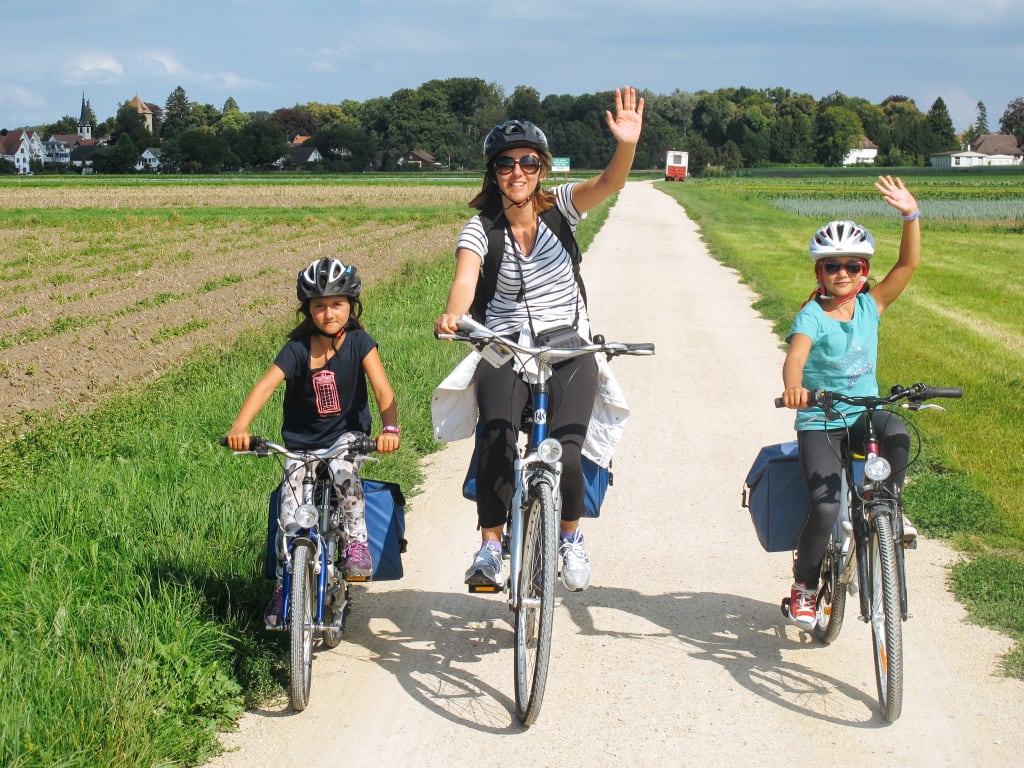 Famiglia che pedala su pista ciclabile in campagna con bambini, viaggio in bici organizzato e vacanza attiva nella natura nel Lago di Costanza
