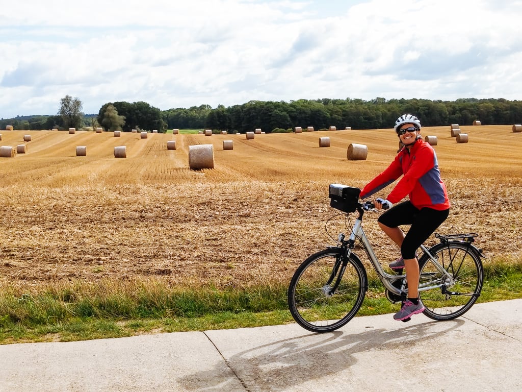 Persona in bicicletta su un sentiero tra campi di grano.