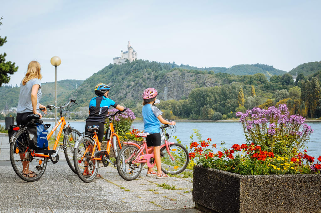 Famiglia in bicicletta sul lungo lago con vista sul castello lungo la ciclabile della Mosella