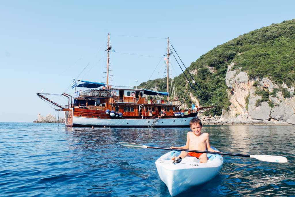Smiling child on a canoe, sailing boat on the blue sea with green hills in the background, boat trips "Girolibero", Ionian Islands, Greece