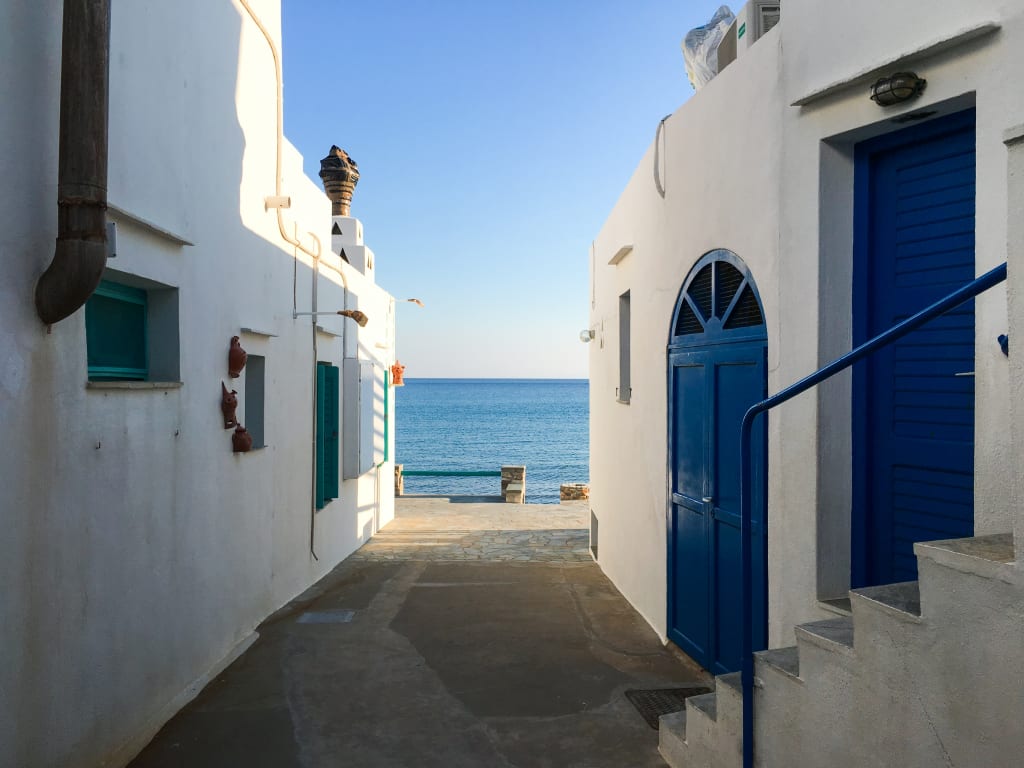 Vicolo stretto con case bianche e porte blu, tipico delle Cicladi. Scorci sul mare, Isole Cicladi