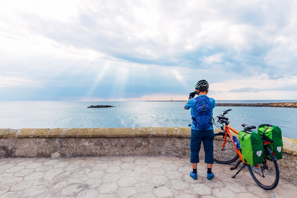Ciclista in viaggio con "Girolibero" scatta una foto da una terrazza panoramica sulla costa vicino a Santa Maria di Leuca, Salento.