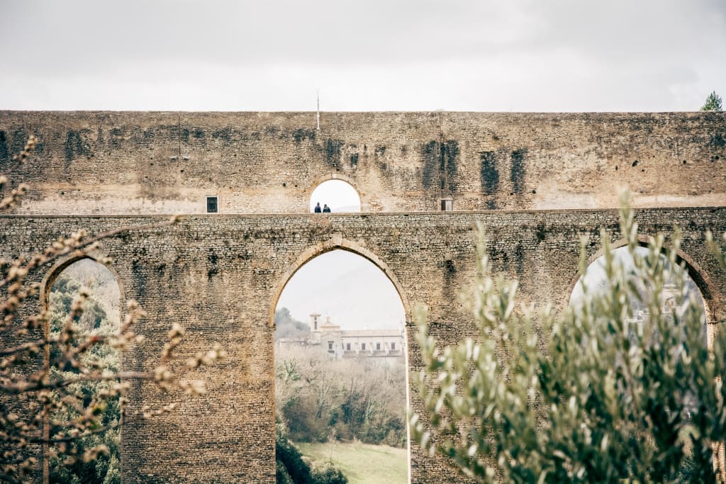 Turisti tra mura medioevali osservano il paesaggio, Umbria, trekking sulla Via di San Francesco