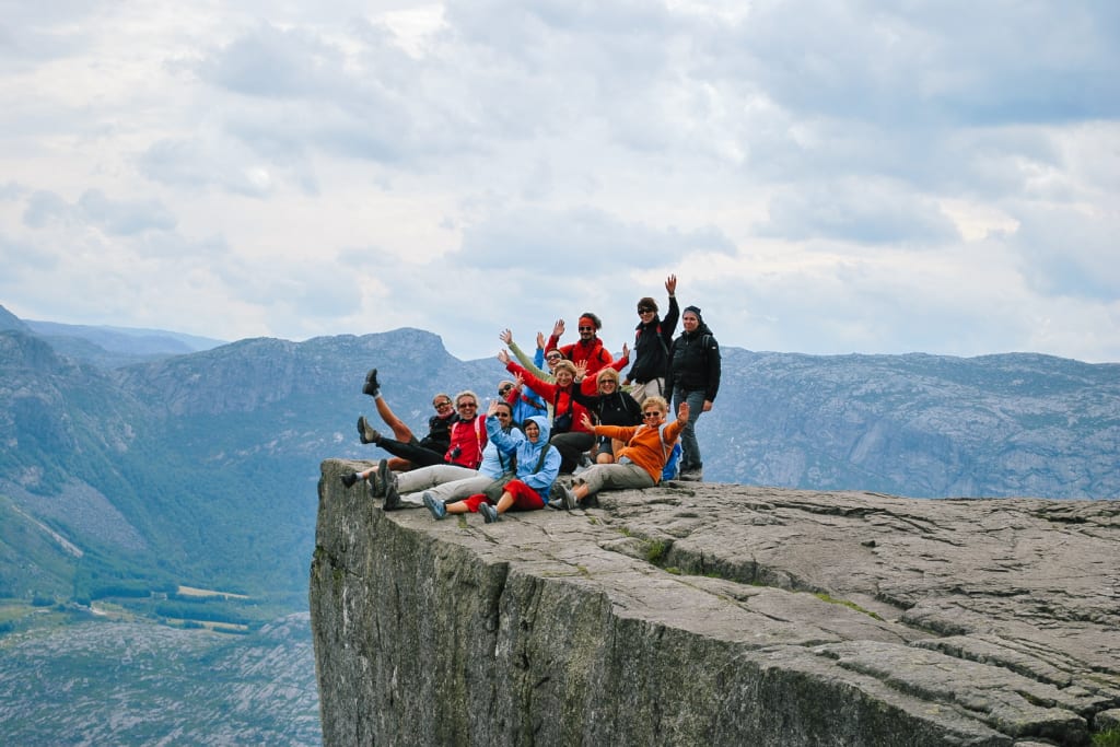 Gruppo di escursionisti seduti sulla cima di Preikestolen con vista sul fiordo, Norvegia, tour dei fiordi norvegesi