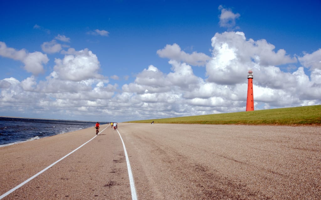 Ampia strada deserta che conduce a un faro rosso vicino al mare.