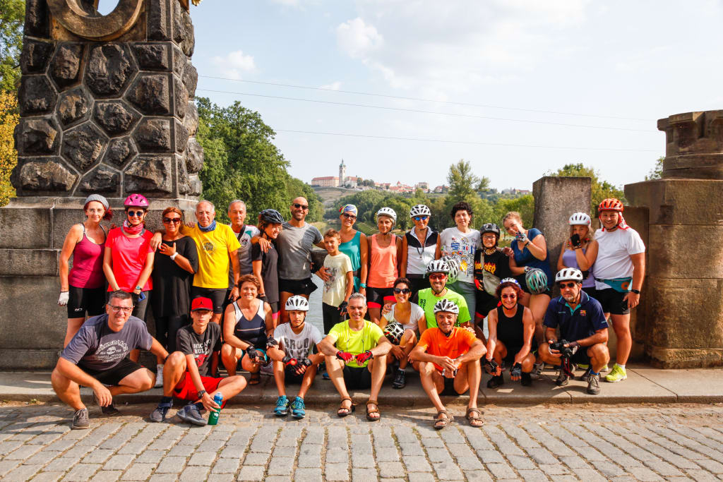 Gruppo di ciclisti in posa davanti a un antico monumento, tour in bici e cultura, la ciclabile dell'Elda e della Moldava