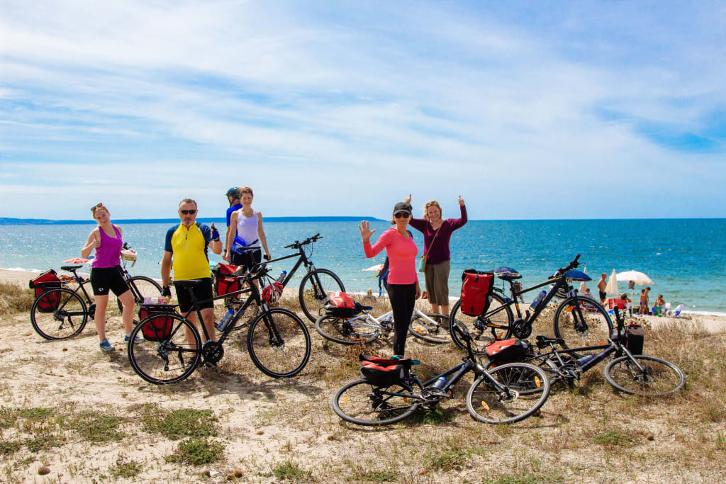 Gruppo di ciclisti in con biciclette in posa su uno scoglio davanti al mare, vacanze in bici in Sardegna