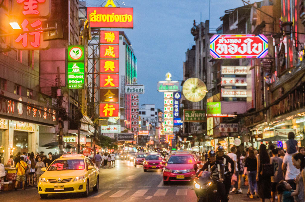 Strada principale di Chinatown Bangkok illuminata da insegne al neon e bancarelle di street food.