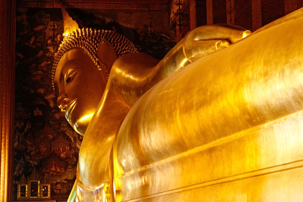 Statua dorata del Buddha Reclino al Wat Pho di Bangkok con dettagli decorativi.