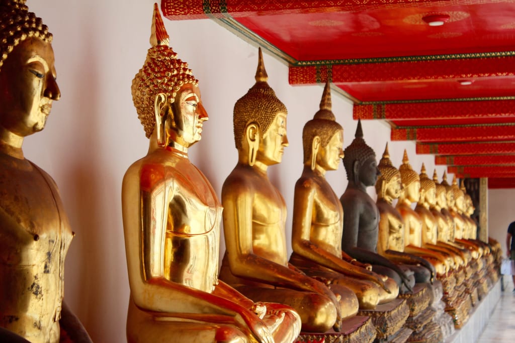 File di statue dorate del Buddha all’interno di un tempio tradizionale thailandese.