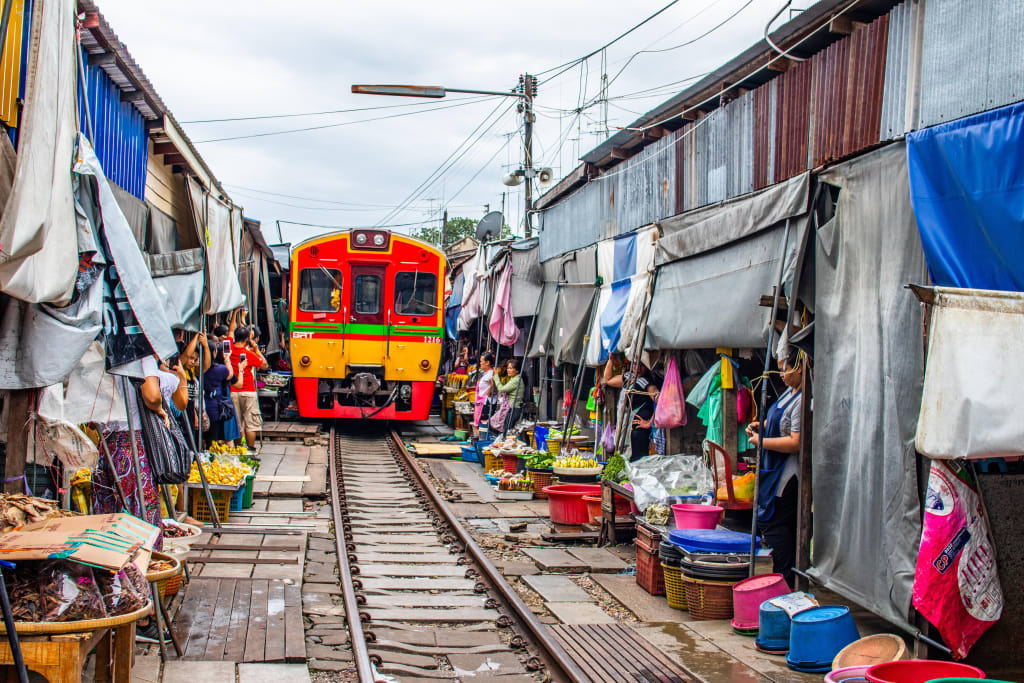 Treno in arrivo al Maeklong Railway Market passando tra bancarelle e venditori locali.