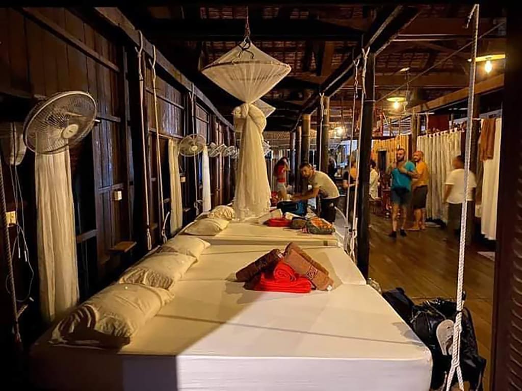 Corridoio serale con letti e zanzariere in lodge su palafitte, atmosfera conviviale del tour culturale in Cambogia