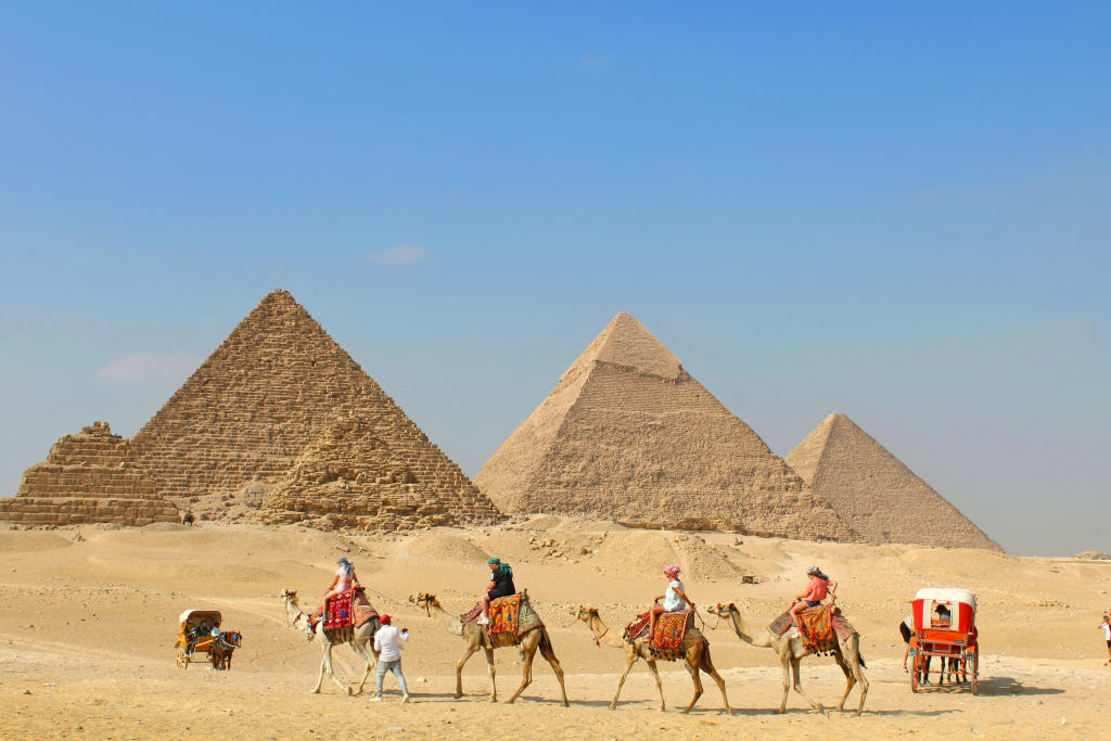 Piramidi di Giza con carovana di cammelli nel deserto, una delle attrazioni più iconiche dell'Egitto.