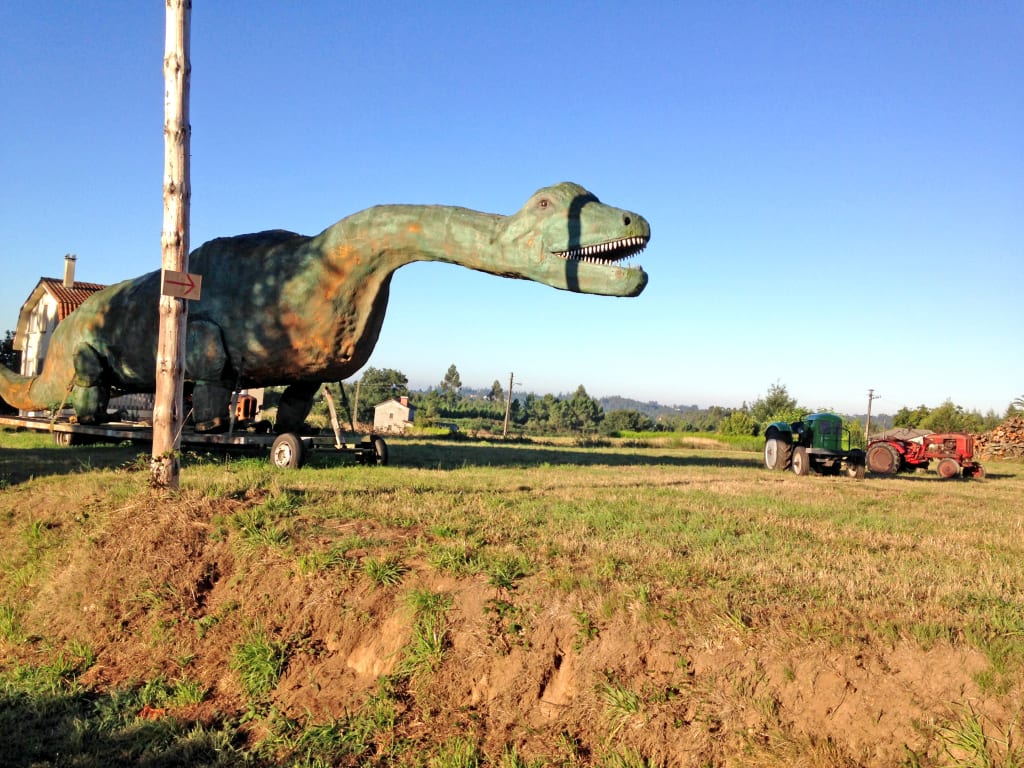 Statua di dinosauro vicino a un tratto rurale del Cammino di Santiago
