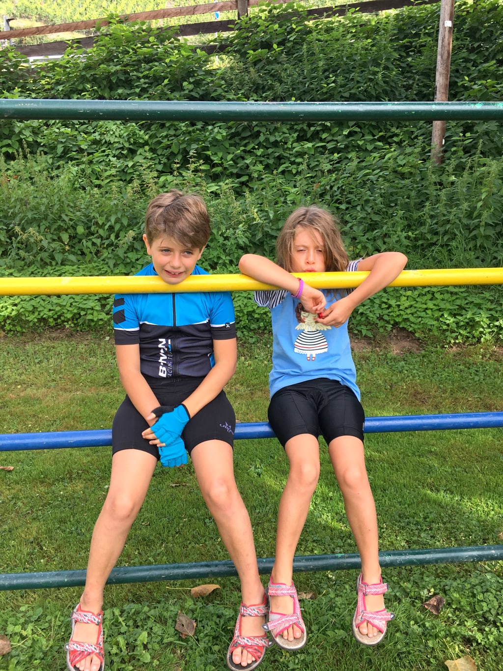 Due bambini seduti su una staccionata lungo un percorso verde, pausa rilassante durante un viaggio slow in famiglia nei Paesi Bassi.