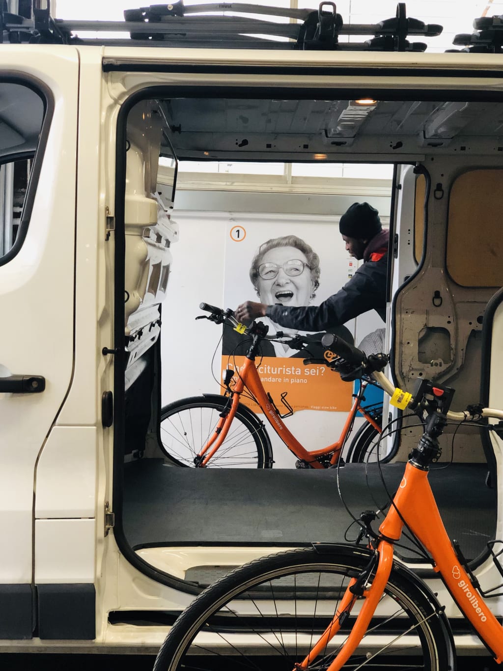 Meccanico carica bicicletta arancione "Girolibero" dentro al furgone della logistica