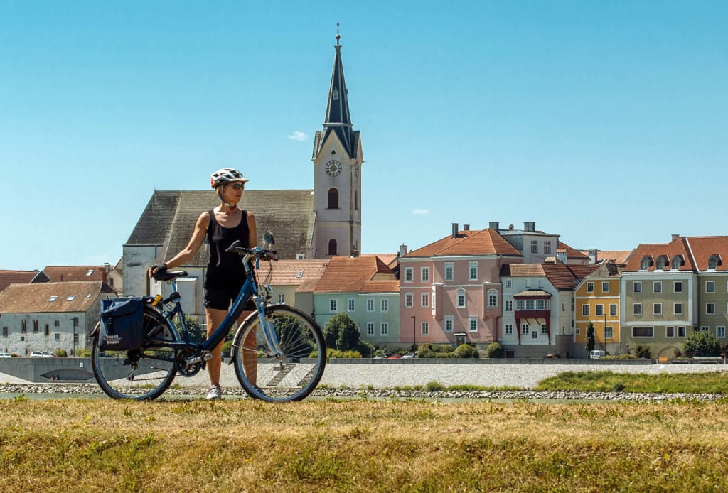 Ciclista in posa con alle spalle la chiesa di St. Stephan, Passau, Germania.