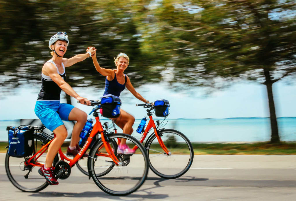 Due cicliste in viaggio con bici arancioni "Girolibero" lungo la ciclovia Alpe Adria