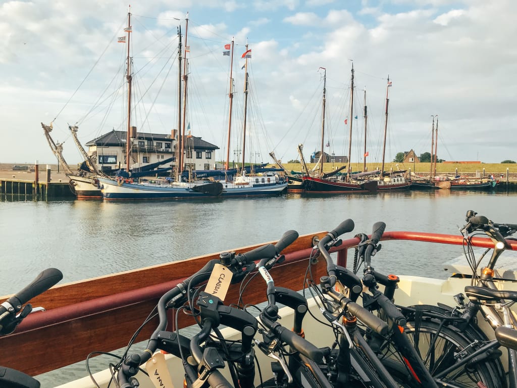 bici appoggiate su un pontile con grandi barche a vela sullo sfondo lungo i canali olandesi della Rotta del Nord