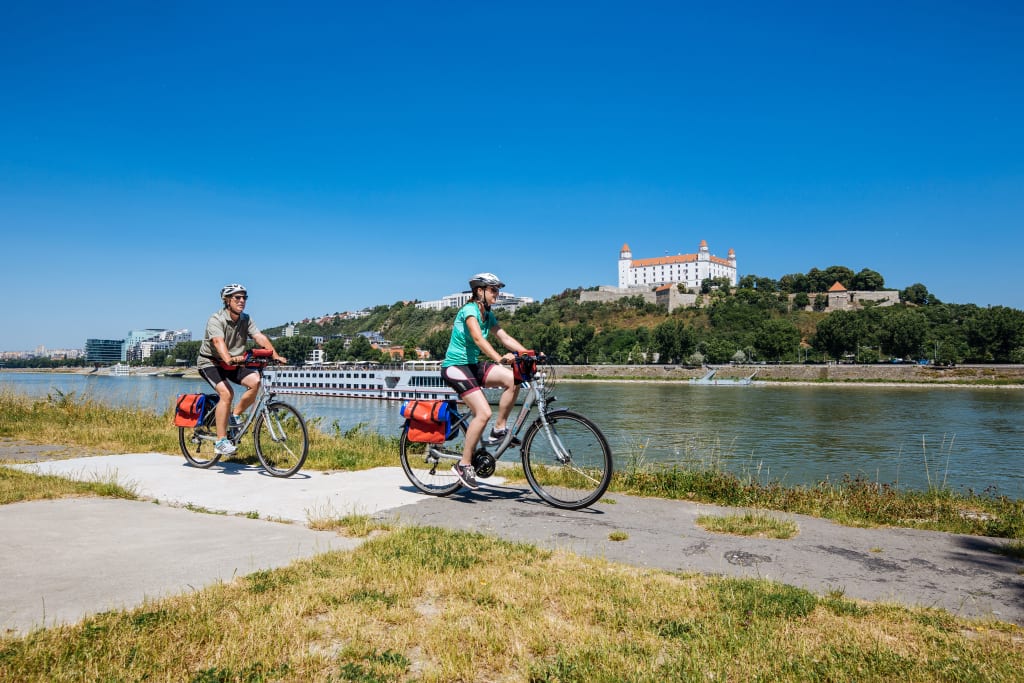 Paesaggio verde lungo la Ciclabile del Danubio con due ciclisti in primo piano