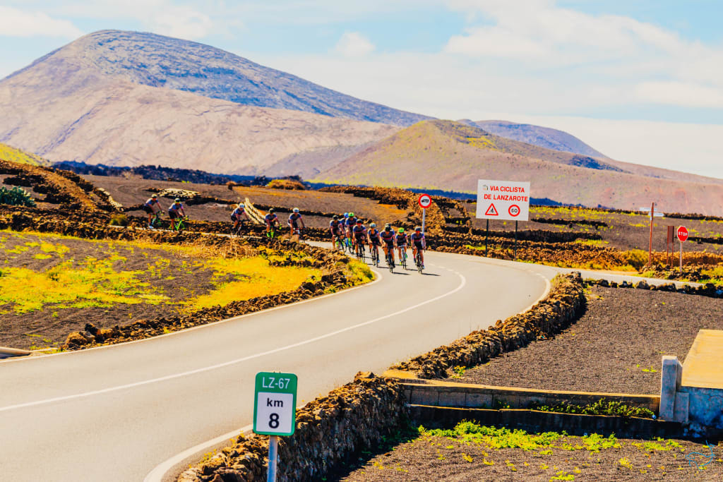 Ciclisti in discesa su una strada di montagna con paesaggio vulcanico a Lanzarote.