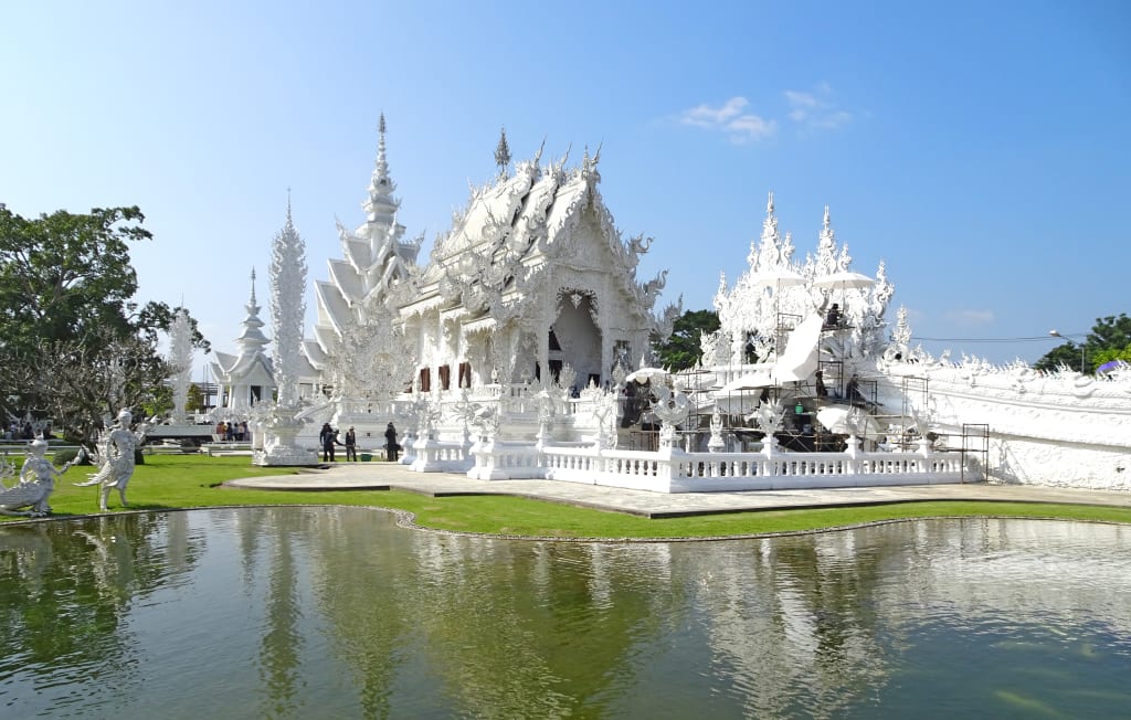 Tempio Bianco Wat Rong Khun a Chiang Rai con architettura moderna riflessa nello stagno.