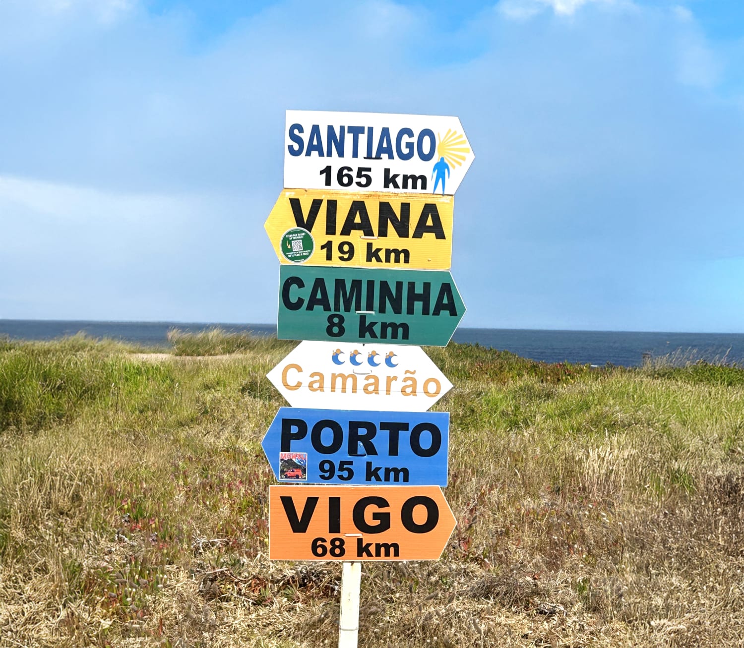 Segnavia colorato del Cammino di Santiago con indicazioni verso Santiago de Compostela, Porto e Vigo, lungo un tratto rurale della Galizia