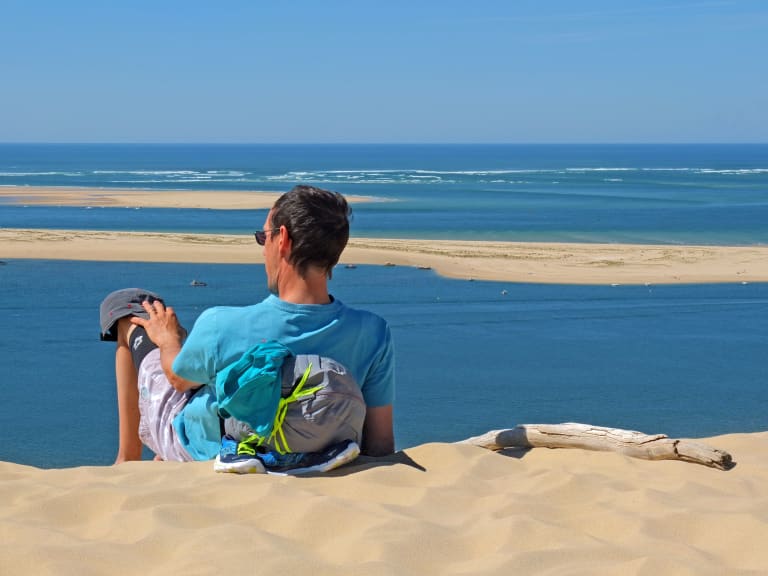 Viaggiatore con zaino seduto su una duna di sabbia con vista sulla baia di Arcachon