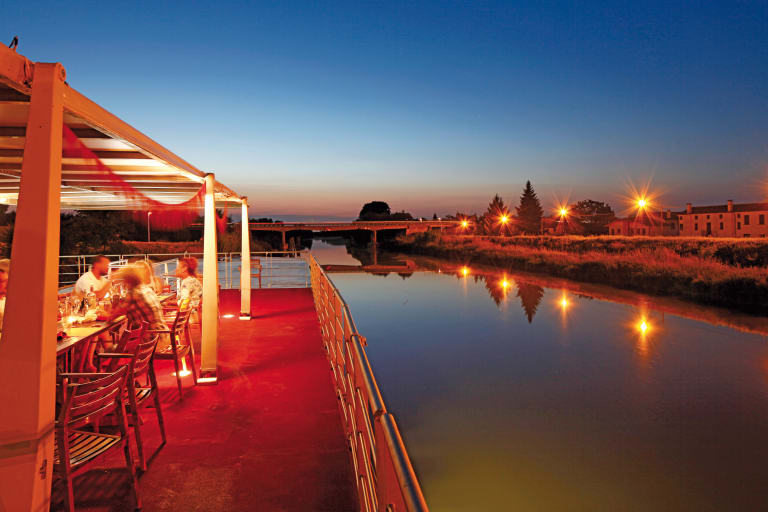 Travellers dining in a boat sailing down the river at night with lights