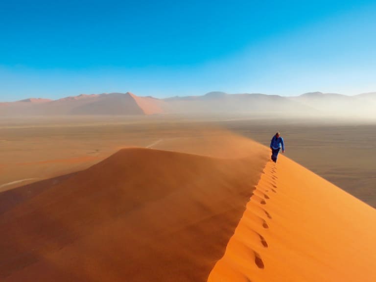 Escursionista che cammina sulla cresta di una duna di sabbia nel deserto della Namibia, viaggiare con 