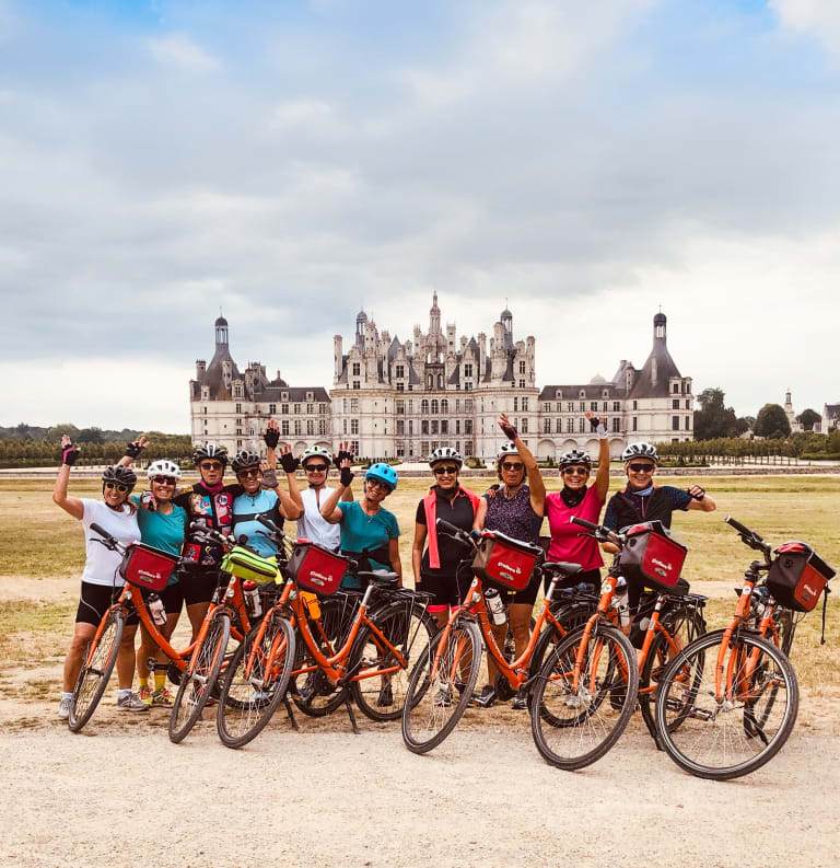 Gruppo di ciclisti davanti a un castello storico europeo nella valle della Loira, tappa culturale durante un itinerario in bicicletta.