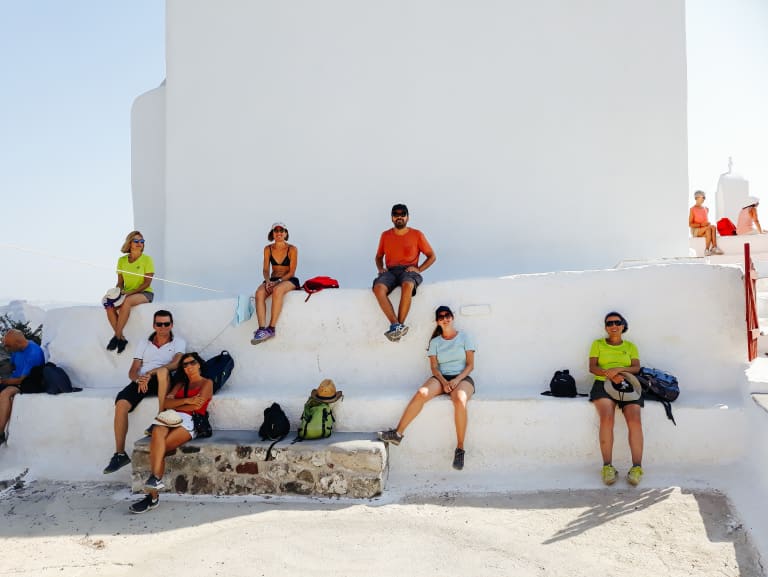 Turisti che si riposano sui gradoni di un muro bianco di Oia a Santorini in viaggio con 
