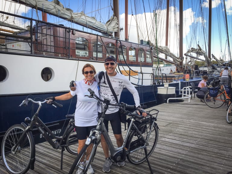 Coppia di ciclisti davanti a una barca ormeggiata nel porto delle Isole Frisone, vacanze in bici e barca 