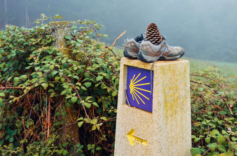 Vecchie scarpe sopra pietra con segnaletica gialla e blu lungo il Cammino di Santiago