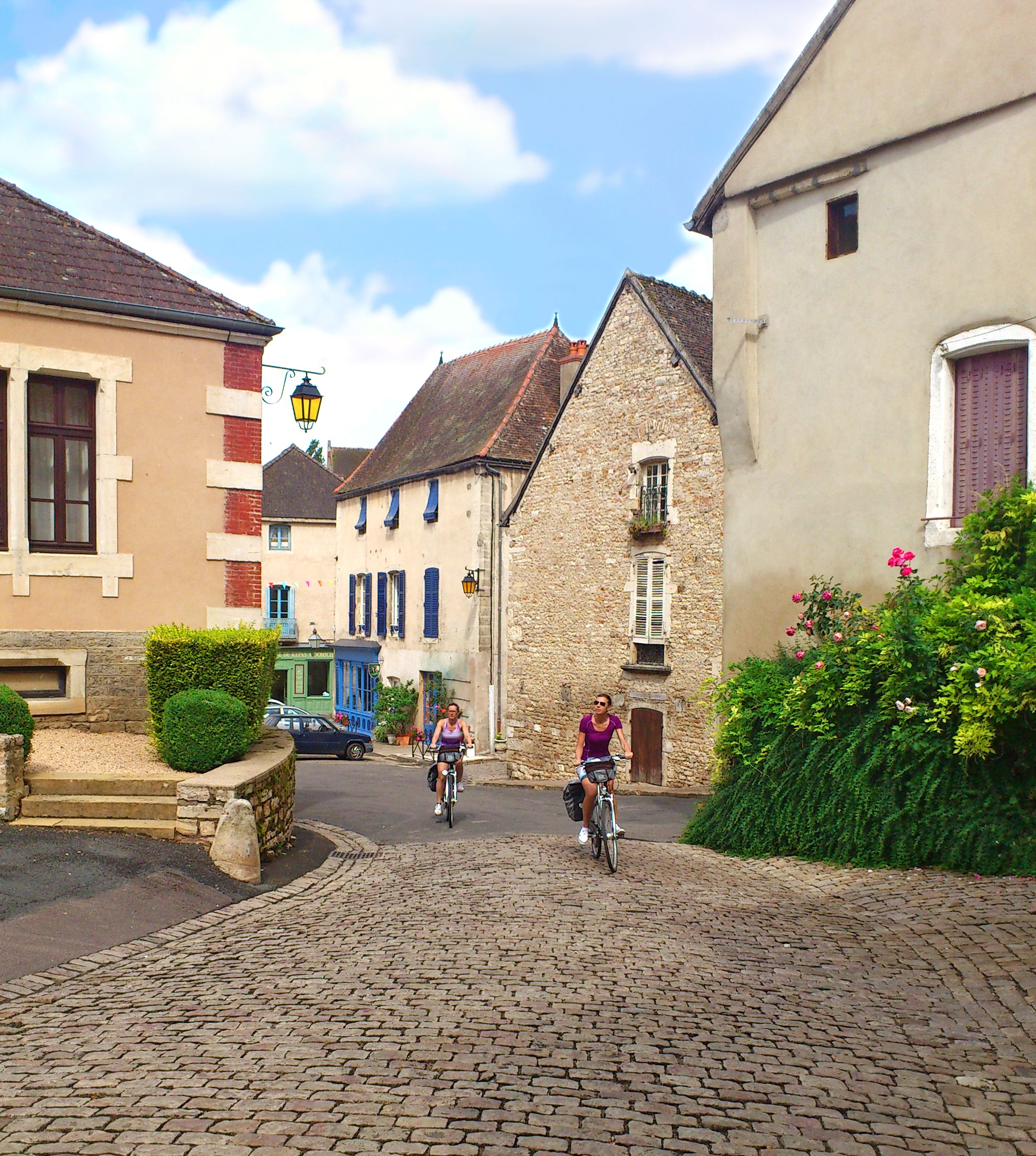 Ciclisti attraversano un villaggio medievale della Borgogna con case in pietra tradizionali, Francia